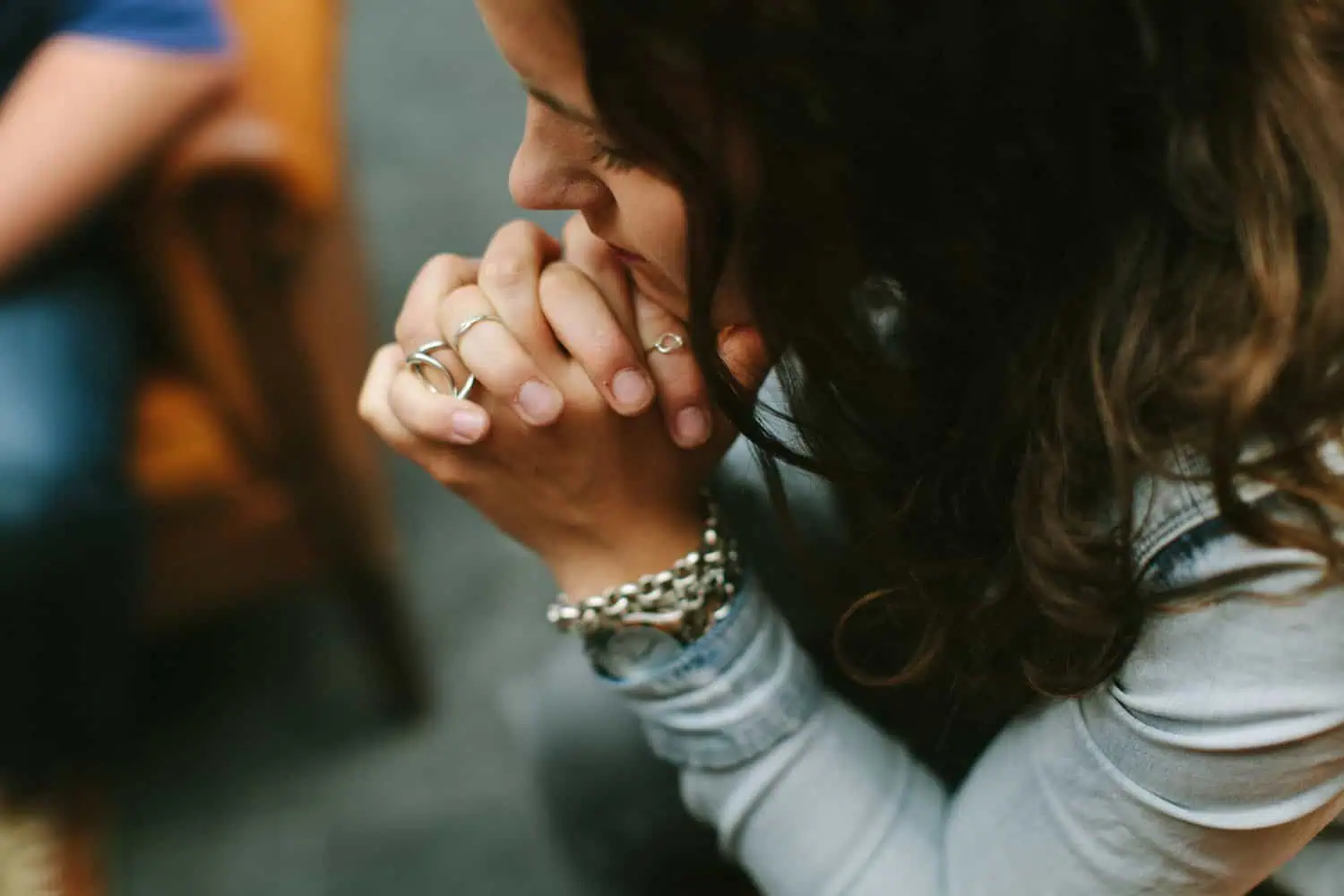 Close-up van een vrouw die haar gevouwen handen voor haar gezicht houdt tijdens het bidden, met ringen en een armband om.